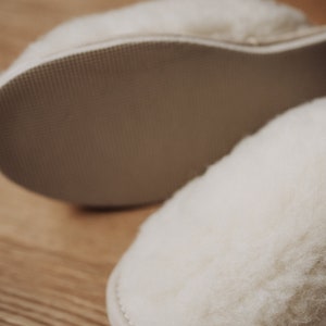 May include: A pair of white sheepskin slippers with a soft, fuzzy texture. The slippers have a rubber sole for traction.