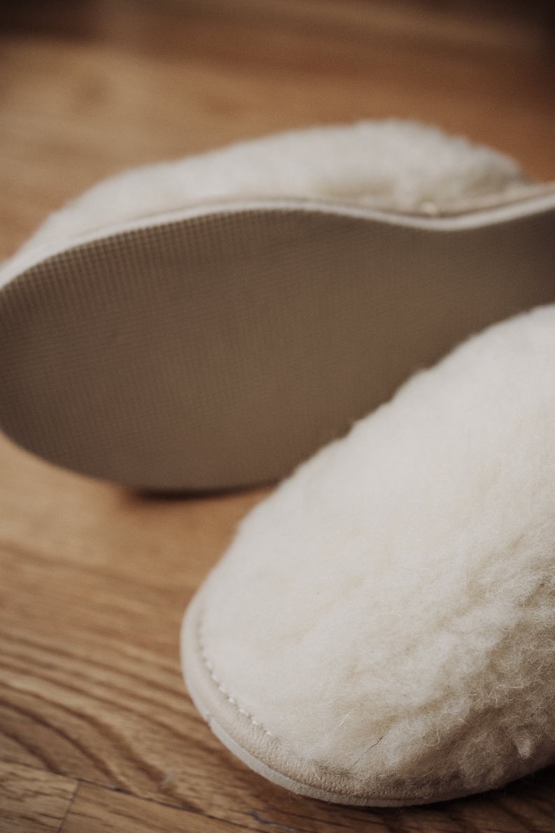 May include: A pair of white sheepskin slippers with a soft, fuzzy texture. The slippers have a rubber sole for traction.