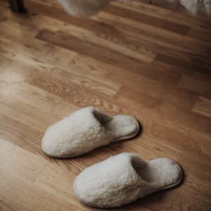 May include: Two pairs of white fluffy slippers on a wooden floor.