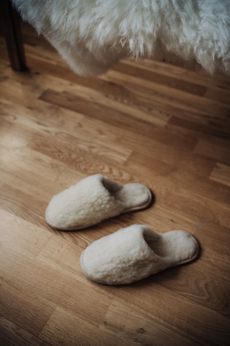 May include: Two pairs of white fluffy slippers on a wooden floor.