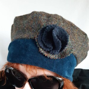 Peut inclure: Un béret en tweed avec un bandeau en daim bleu foncé et une fleur assortie. Le béret est un mélange de fils bruns, bleus et oranges. Le modèle porte des lunettes de soleil noires.