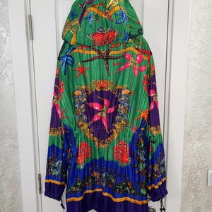 May include: A hooded jacket featuring a vibrant, pleated fabric with a colorful marine-themed print. The design includes starfish, seashells, and ornate gold-toned circular patterns against a background of bright green, blue, and purple hues.