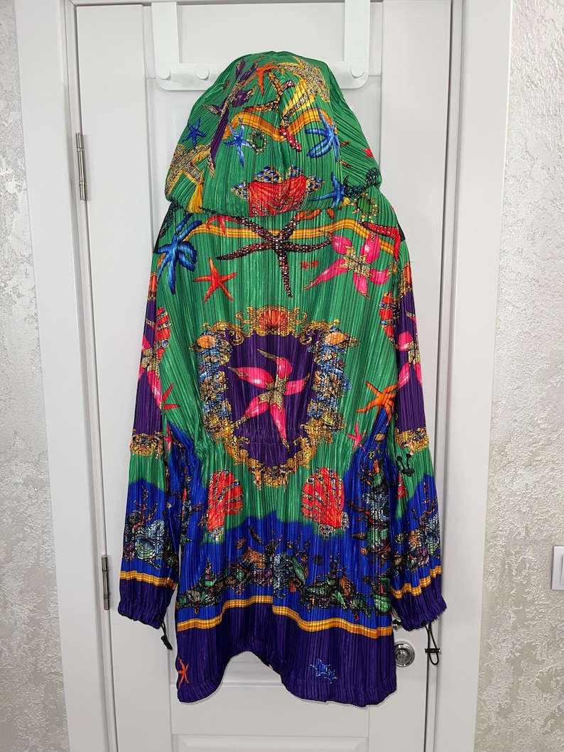 May include: A hooded jacket featuring a vibrant, pleated fabric with a colorful marine-themed print. The design includes starfish, seashells, and ornate gold-toned circular patterns against a background of bright green, blue, and purple hues.