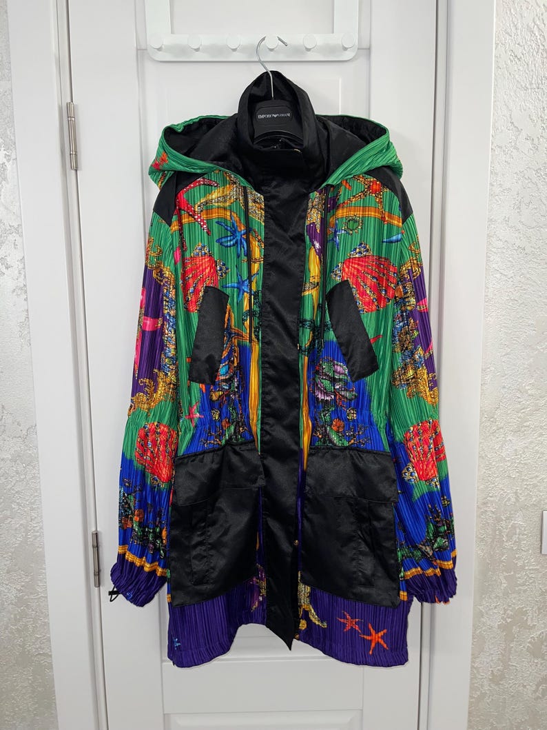 May include: A hooded jacket featuring a vibrant, pleated fabric with a colorful marine-themed print of seashells, starfish, and coral in shades of green, blue, yellow, and red. The jacket includes solid black panels, a front zipper, and pockets.