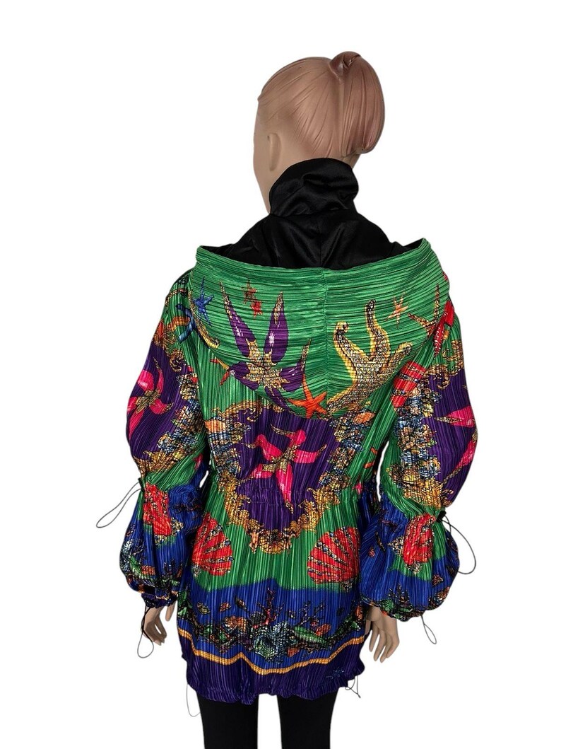 May include: A long-sleeved hooded jacket featuring a vibrant, pleated fabric with a colorful marine-themed print. The design includes starfish, seashells, and coral motifs in shades of green, purple, blue, red, and gold, with adjustable drawstrings.