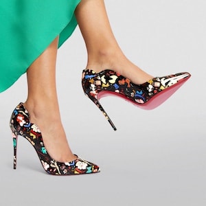May include: Black high-heeled pumps with a colorful cartoon print. The shoes have a pointed toe, a thin stiletto heel, and a signature red sole. The heels are approximately 4 inches (10 cm) high.