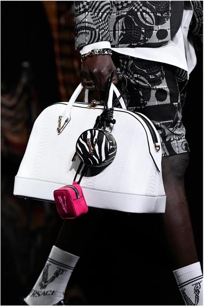 Puede incluir: Bolso de mano de cuero blanco con un patr&oacute;n texturizado, cremallera negra y herrajes dorados. Un peque&ntilde;o bolso redondo con estampado de cebra y un mini bolso rosa est&aacute;n adjuntos. Accesorio de moda.