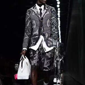 Puede incluir: Un traje con estampado en blanco y negro, compuesto por una americana y un pantal&oacute;n corto, se lleva con una camisa blanca y una corbata negra. El conjunto se completa con zapatos negros y calcetines blancos. Se lleva un bolso de mano blanco con detalles en negro.