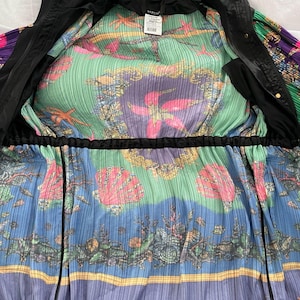 May include: A black hooded jacket with a vibrant, pleated interior lining featuring a colorful marine-themed print. The pattern displays pink starfish, seashells, and coral motifs against green and blue backgrounds, with a Versace brand label.
