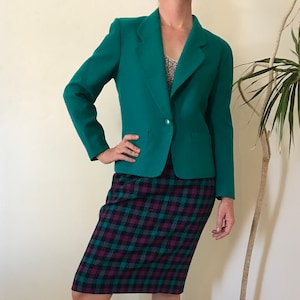 May include: A teal blazer with a single button closure and a plaid skirt. The skirt has a black, green, and purple plaid pattern.
