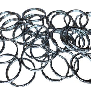 May include: A collection of shiny, silver-colored split key rings. The rings are circular and made of metal. A small white label with the text "CROWN KIRK INDUSTRIAL" and an American flag is in the lower left corner.