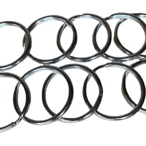 May include: A collection of ten shiny, silver-colored key rings. The rings are circular and made of metal. A small white label with text and an American flag is in the lower left corner.