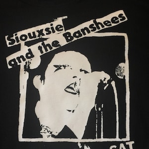 Op de afbeelding: Zwart-wit grafisch T-shirt met de tekst "Siouxsie and the Banshees" en "Erie's" met de datum "SAT MAY 14" erop gedrukt.
