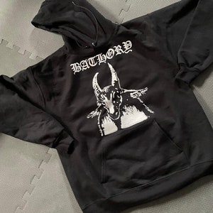 May include: Black hooded sweatshirt with a white graphic print of a goat's head and the word "BATHORY" in a gothic font.