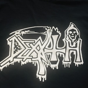 Może przedstawiać: Czarny T-shirt z białym nadrukiem słowa "DEATH" w stylu kroju kroplowego. Grafika zawiera również postać w kapturze z czaszką.