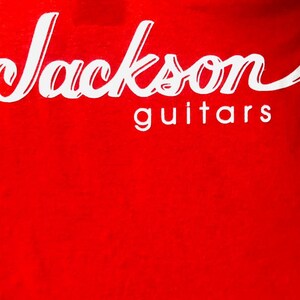 May include: Red t-shirt with white text that reads "Jackson guitars".