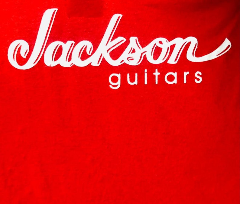 May include: Red t-shirt with white text that reads "Jackson guitars".
