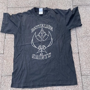 Puede incluir: Camiseta negra con un gráfico blanco de un tridente y el texto "Battalion of Saints".