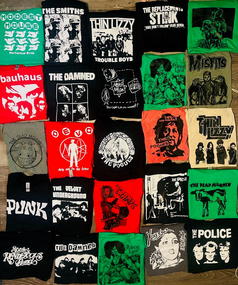May include: A selection of band t-shirts featuring logos and artwork from bands like The Smiths, Thin Lizzy, and The Damned. The shirts are in various colours, including black, white, red, and green. The shirts are displayed flat.