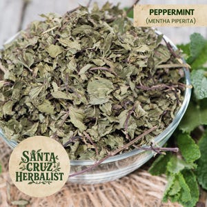 May include: A clear glass bowl filled with dried peppermint leaves and stems. The leaves are a mix of green and brown, with a few purple stems visible. The text "Peppermint (Mentha Piperita)" is in the upper right corner. The Santa Cruz Herbalist logo is in the lower left.