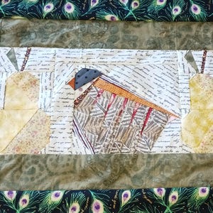 以下が含まれることがあります： 鳥と梨のデザインが特徴のキルトテーブルランナー。鳥は青い頭、オレンジ色のくちばし、茶色と灰色の体を持っています。梨は花柄の黄色です。ボーダーは緑色です。