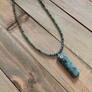May include: A green gemstone necklace with a silver chain and a rectangular pendant. The pendant is made of a green gemstone with a mottled pattern.