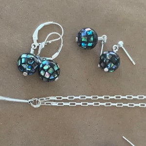 May include: A silver necklace with a black and green abalone shell pendant. Matching earrings with black and green abalone shell drops are also included.