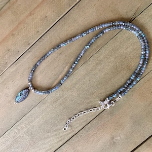 May include: A silver chain necklace with a blue and green abalone shell pendant and a silver clasp. The necklace is made of small, round beads.
