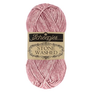 Peut inclure: Une pelote de laine Scheepjes Stone Washed de couleur rose poudré. La laine a un aspect doux et texturé avec un mélange de fibres roses et blanches. L'étiquette indique "Scheepjes STONE WASHED" dans une police décorative.