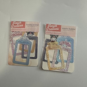 May include: Two packs of colorful, glittery photo card holder stickers featuring Sanrio characters. The stickers are labeled "sanrio holder photo card deco stickers" and "hand-made sticker pack".