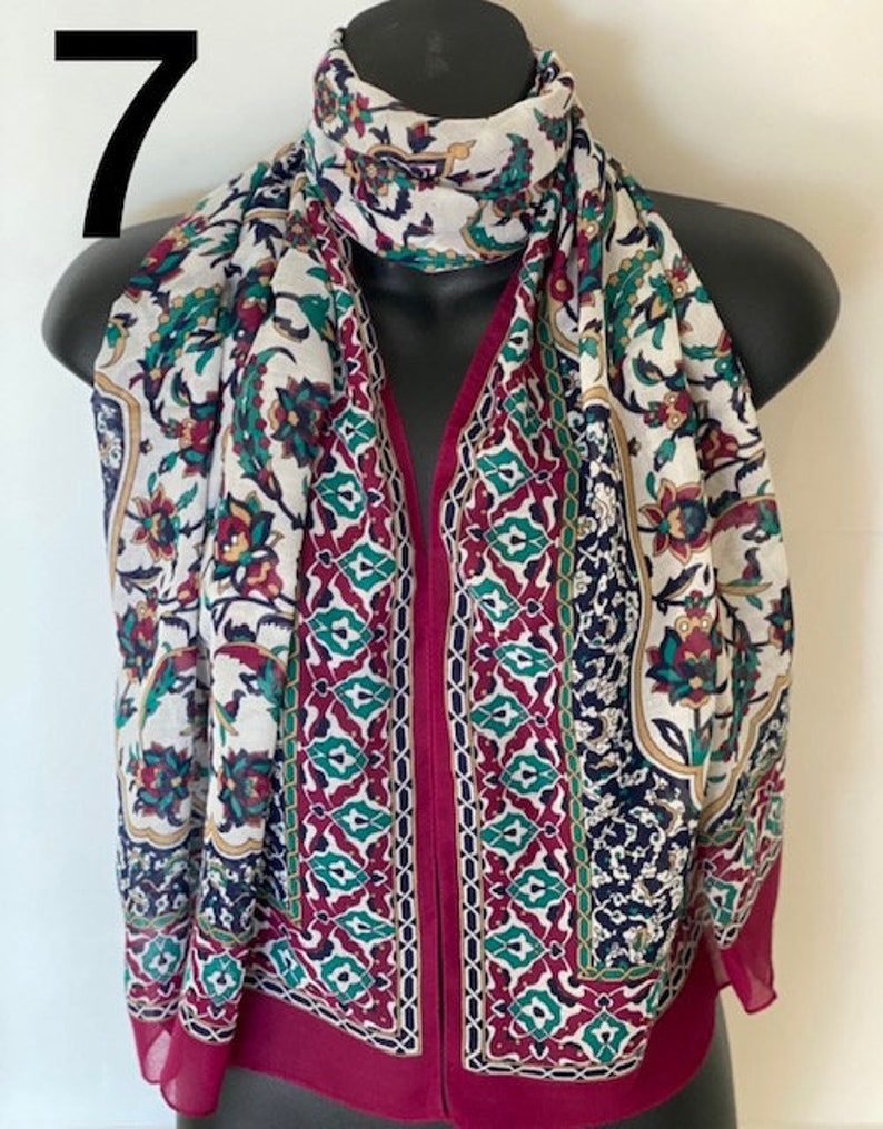 Peut inclure: Une &eacute;charpe &agrave; motifs blancs et bordeaux avec un design g&eacute;om&eacute;trique. L'&eacute;charpe pr&eacute;sente un motif floral avec des accents verts, rouges et bleus.