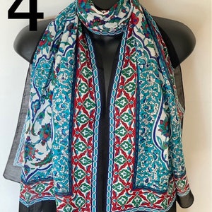 Peut inclure: Une &eacute;charpe &agrave; motifs blancs, bleus, rouges et verts avec une bordure noire. L'&eacute;charpe est faite d'un tissu l&eacute;ger et pr&eacute;sente un motif g&eacute;om&eacute;trique.
