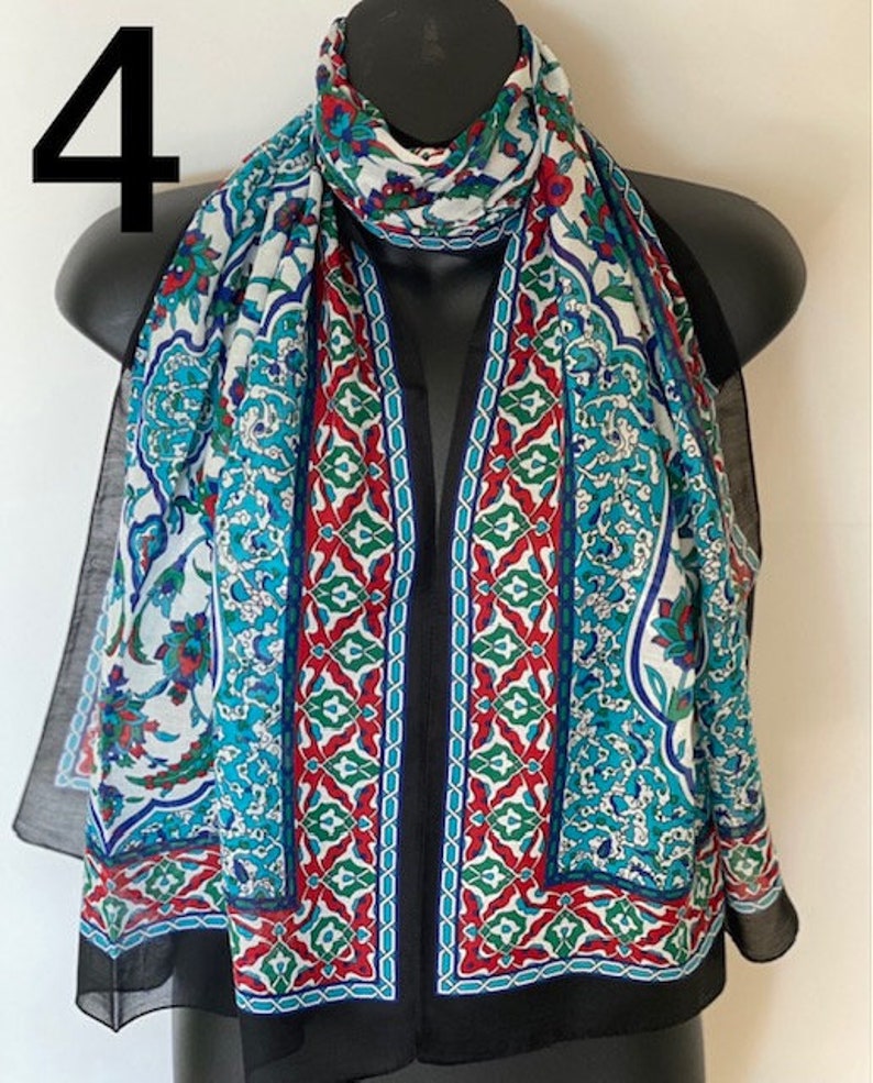 Peut inclure: Une &eacute;charpe &agrave; motifs blancs, bleus, rouges et verts avec une bordure noire. L'&eacute;charpe est faite d'un tissu l&eacute;ger et pr&eacute;sente un motif g&eacute;om&eacute;trique.
