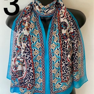 Peut inclure: Une &eacute;charpe bleu turquoise avec un motif blanc, marron et rouge. Le motif pr&eacute;sente des formes g&eacute;om&eacute;triques et des motifs floraux.