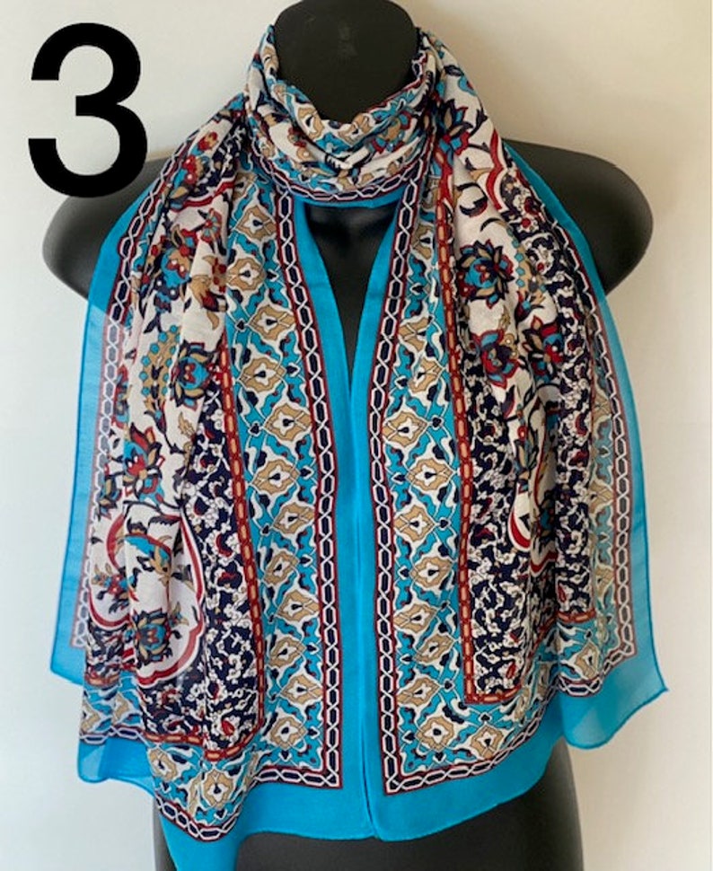 Peut inclure: Une &eacute;charpe bleu turquoise avec un motif blanc, marron et rouge. Le motif pr&eacute;sente des formes g&eacute;om&eacute;triques et des motifs floraux.
