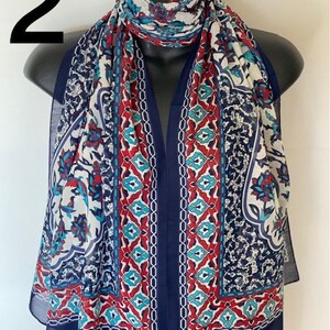 Peut inclure: Une &eacute;charpe &agrave; motifs g&eacute;om&eacute;triques bleus, rouges, blancs et turquoise. L'&eacute;charpe est pli&eacute;e et drap&eacute;e sur un mannequin.