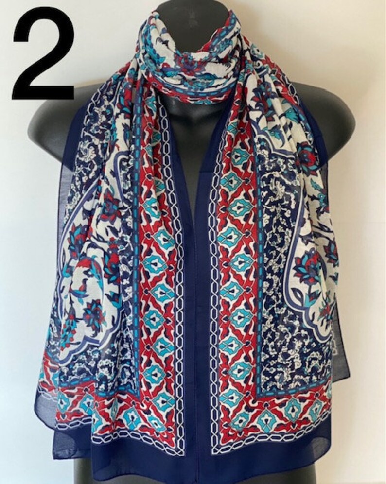 Peut inclure: Une &eacute;charpe &agrave; motifs g&eacute;om&eacute;triques bleus, rouges, blancs et turquoise. L'&eacute;charpe est pli&eacute;e et drap&eacute;e sur un mannequin.