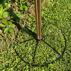 May include: A copper-colored metal stand with a black metal base. The base has a circular shape with spokes radiating out from the center.