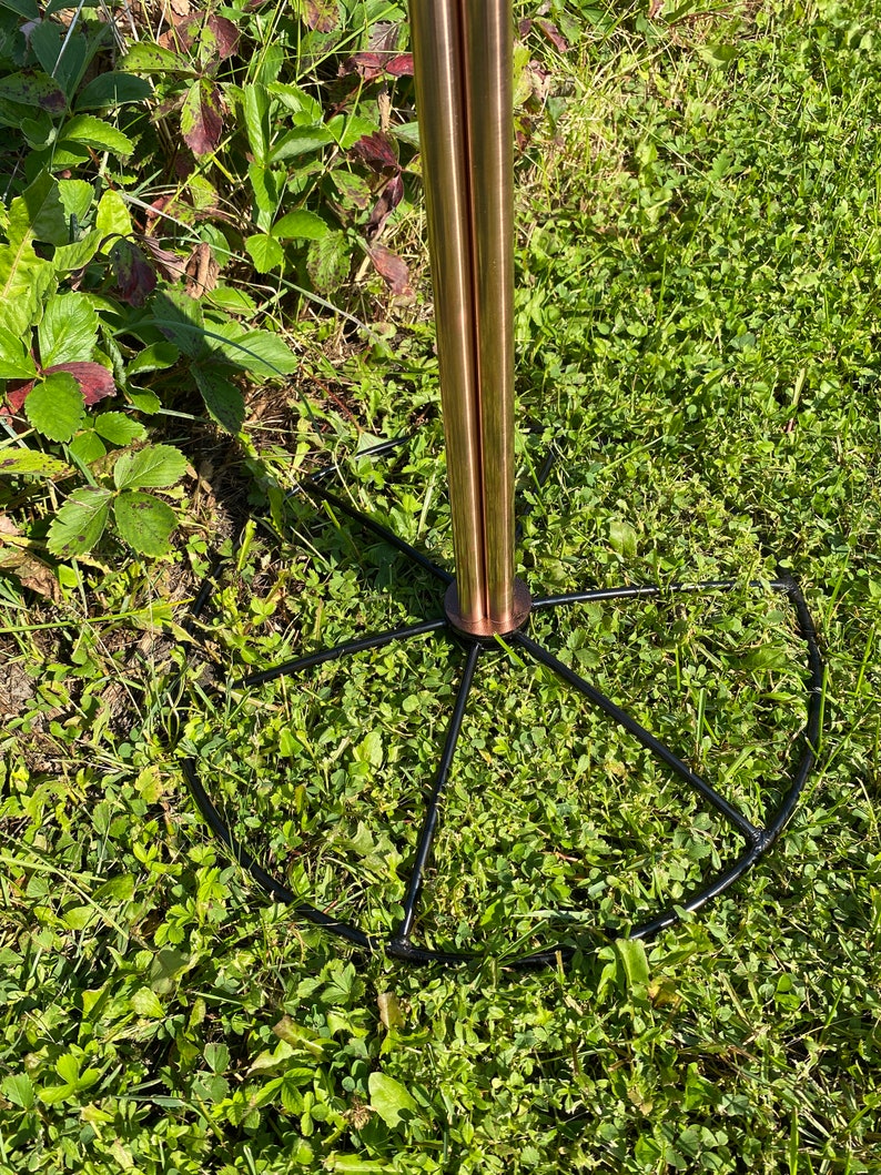 May include: A copper-colored metal stand with a black metal base. The base has a circular shape with spokes radiating out from the center.