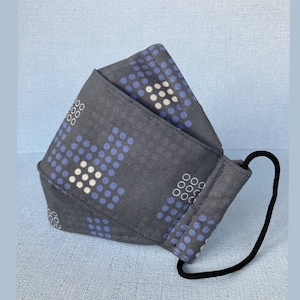 May include: A grey fabric face mask with a blue and white polka dot pattern. The mask has a black elastic band.