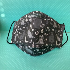 K&ouml;nnte beinhalten: Schwarze Gesichtsmaske mit einem wei&szlig;en Muster aus Waschb&auml;ren, B&auml;umen und M&uuml;lleimern.