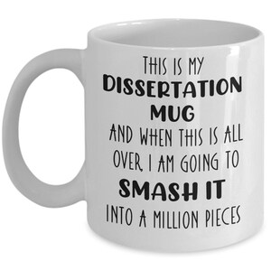 May include: White ceramic mug with a curved handle. The mug features black text that reads: "THIS IS MY DISSERTATION MUG AND WHEN THIS IS ALL OVER, I AM GOING TO SMASH IT INTO A MILLION PIECES."