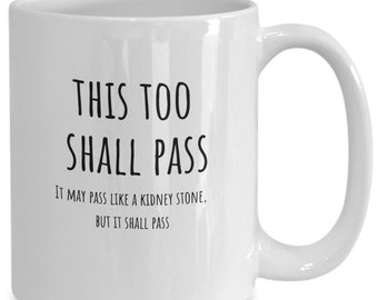 May include: White ceramic coffee mug with black text that reads "This too shall pass. It may pass like a kidney stone, but it shall pass."