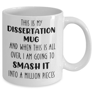 May include: White ceramic mug with the text "THIS IS MY DISSERTATION MUG AND WHEN THIS IS ALL OVER, I AM GOING TO SMASH IT INTO A MILLION PIECES" in black. The mug has a curved handle.