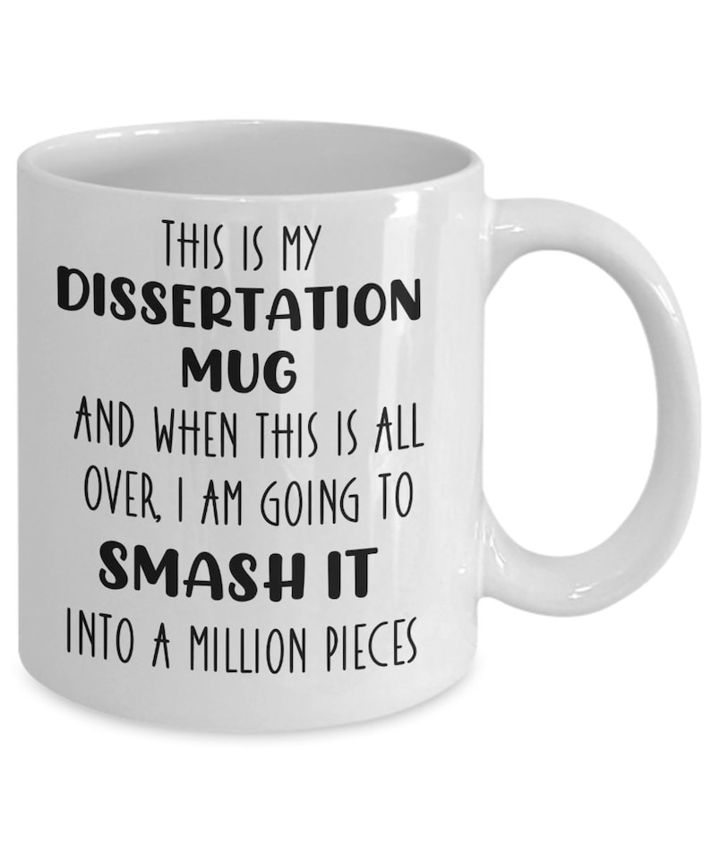 May include: White ceramic mug with the text "THIS IS MY DISSERTATION MUG AND WHEN THIS IS ALL OVER, I AM GOING TO SMASH IT INTO A MILLION PIECES" in black. The mug has a curved handle.
