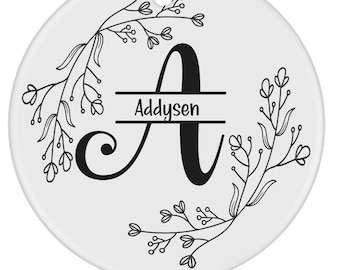 Puede incluir: Un adorno de cerámica blanca con un diseño floral negro y la letra "A" en el centro. El nombre "Addysen" está escrito en una pancarta debajo de la letra.