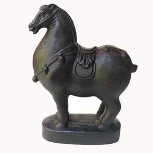 Pode incluir: Estatueta de cavalo castanho escuro com sela. O cavalo está em pé sobre uma pequena base redonda. A estatueta tem detalhes, incluindo crina, cauda e freio. É um item decorativo.
