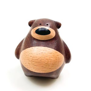 Puede incluir: Una figura de oso de madera hecha a mano con un cuerpo marrón oscuro y una barriga marrón claro. El oso tiene una nariz negra y un diseño simple y redondeado. La figura es un artículo decorativo.