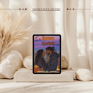 Puede incluir: Una tableta digital que muestra la portada de una novela rom&aacute;ntica titulada "Love Notes" de Kismet St. James. La portada presenta a una pareja abraz&aacute;ndose contra un horizonte urbano al atardecer.