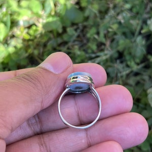 Op de afbeelding: Een zilveren ring met een lichtblauwe ovale edelsteen in een bezel-setting.